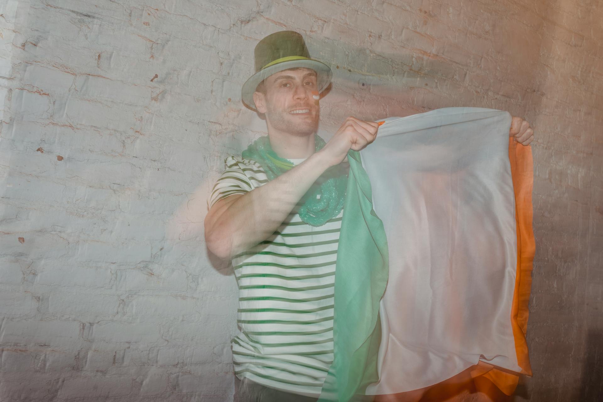 Adult male in shamrock hat with national flag of Ireland looking at camera on St Paddys Day behind glass wall