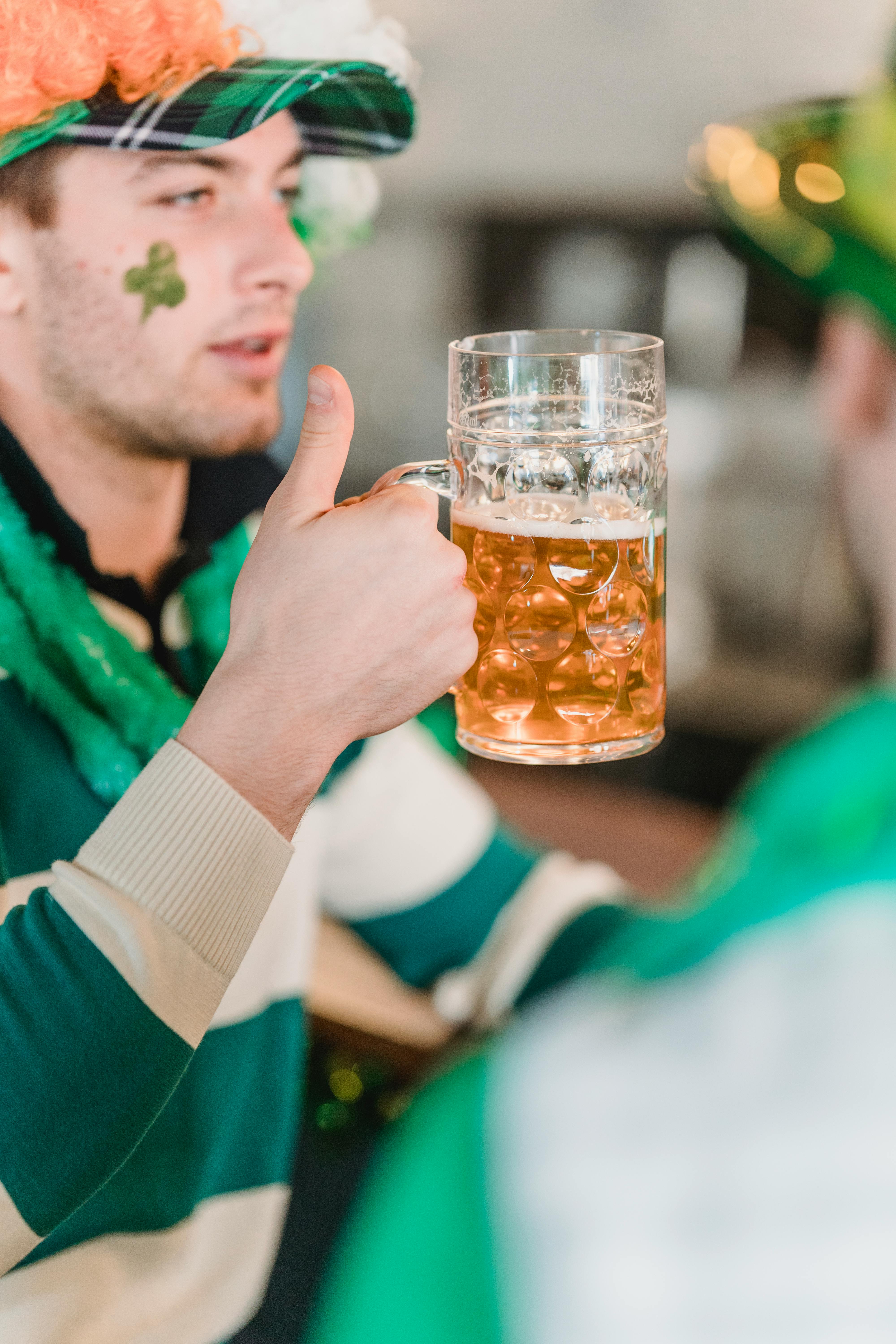 man with green clover on face and beer in hands