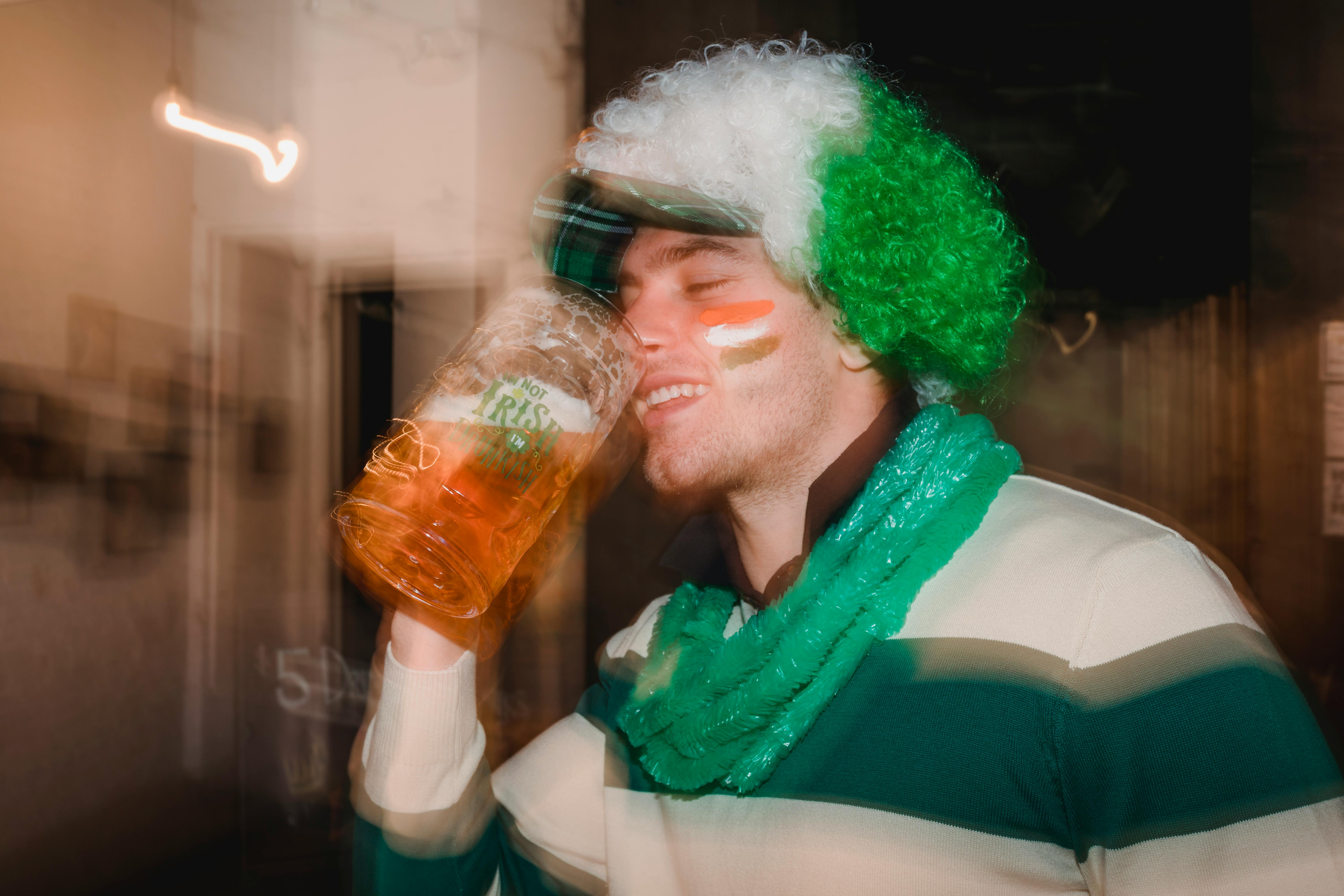 happy man with irish flag on face drinking beer