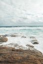 Picturesque view of azure foamy sea waves washing rocky stony coast under cloudy sky