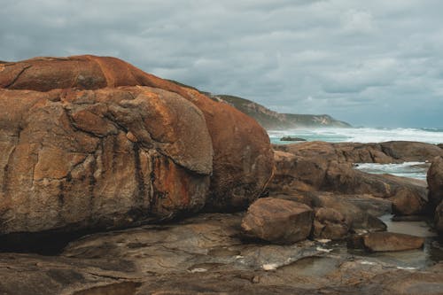 Rough rocky seashore with massive stones near stormy azure sea waving under gloomy cloudy sky