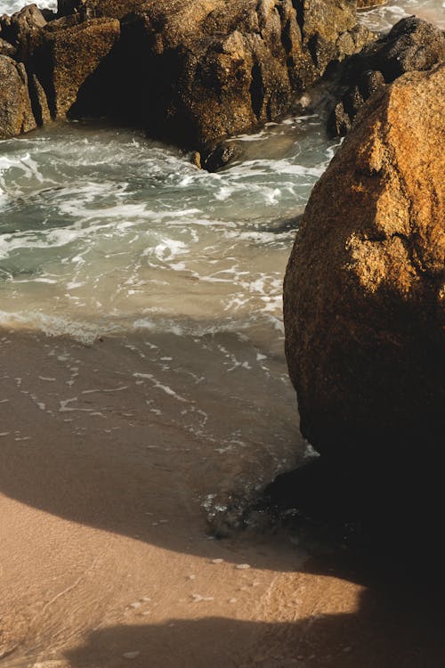 Massive rough stones on sandy beach washed by foamy azure sea in sunlight