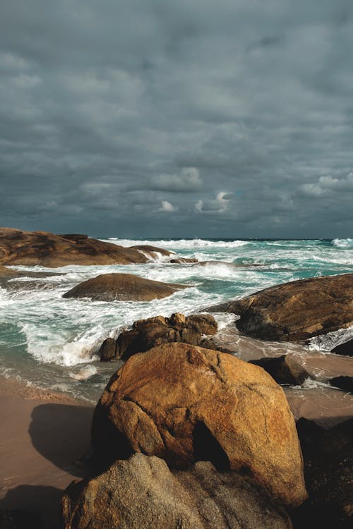 Free Scenery of dramatic cloudy sky above blue shallow sea waving on stony rough shore on overcast day Stock Photo