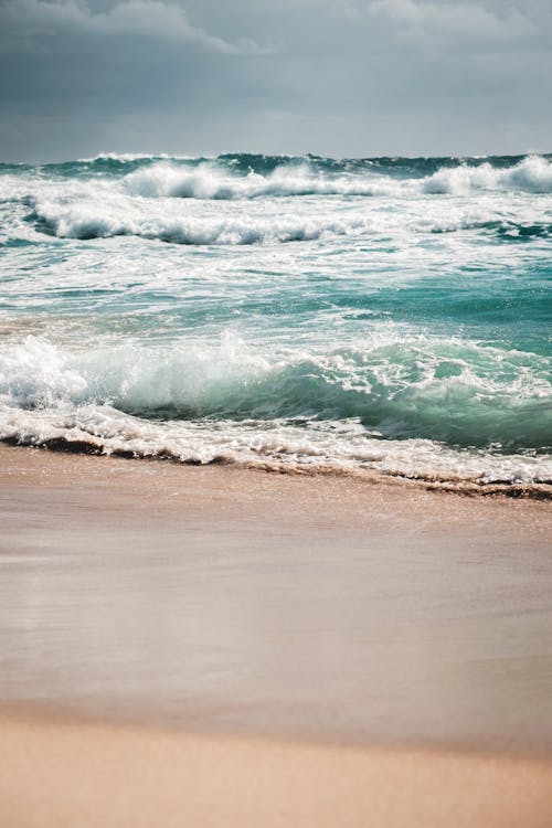 Amazing view of stormy azure sea with foamy waves rolling on wet sandy beach on cloudy overcast day