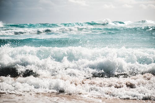 Turquoise stormy sea with foamy waves splashing on sandy beach against cloudy sky