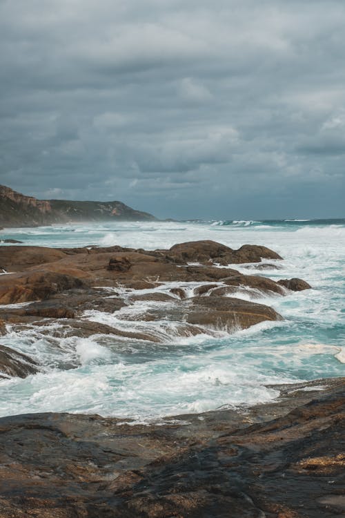 Rocky cliff washed by stormy sea on gloomy weather