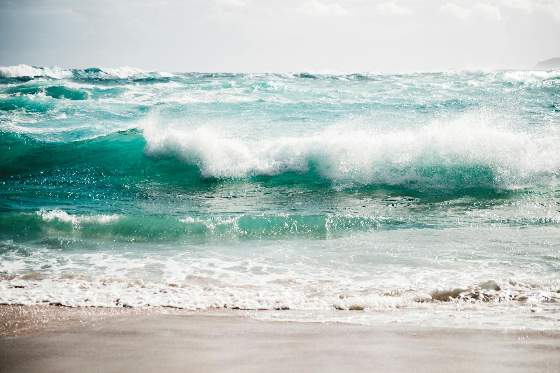 Dynamic ocean waves crashing onto a pristine sandy beach under bright daylight.