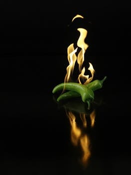Dynamic image of green chili peppers engulfed in flames over a dark reflective surface.
