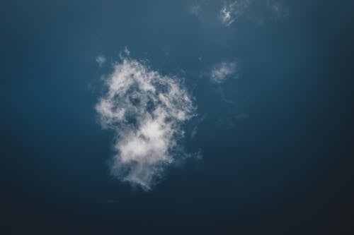 Low angle of small white fluffy cloud soaring in clear blue sky in sunlight