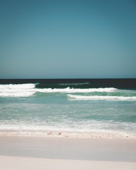 Picturesque wavy water of ocean washing sand of shore under cloudless blue sky