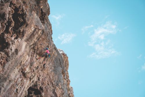 Free From below of anonymous person climbing on high stony rough cliffs in bright sunlight Stock Photo