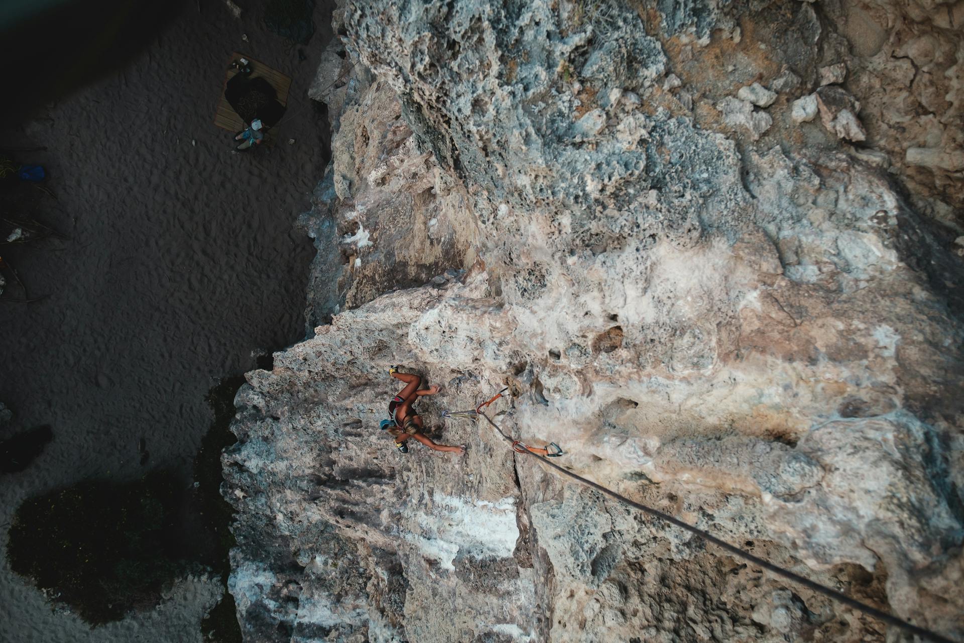 Top view of anonymous tourist with rope climbing on rough stony terrain in daytime