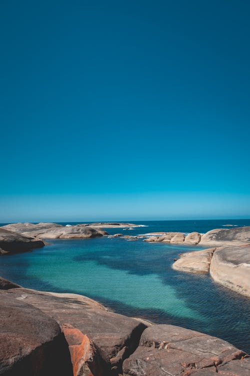 Stony shore washed by azure water of sea in coastal area against clear blue sky in nature on sunny summer day