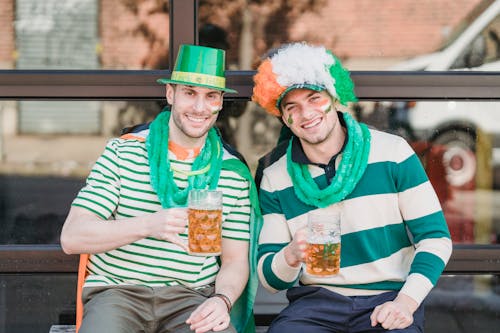 Smiling guy in festive outfits enjoying refreshing beer in street cafe