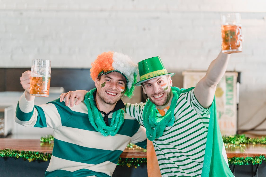 Excited young male friends raising glasses of beer while celebrating St Patricks Day