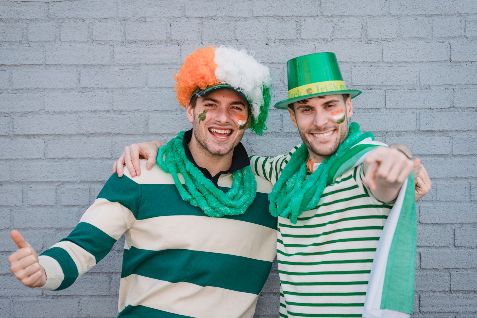 Delighted male friends in traditional colorful hats and flags of Ireland painted on faces looking at
