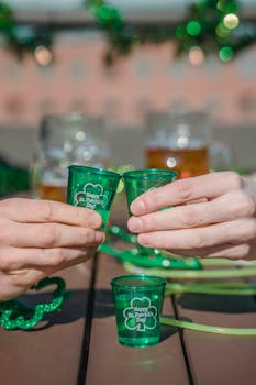 Hands clink green shot glasses in a festive St. Patrick's Day celebration outdoors.