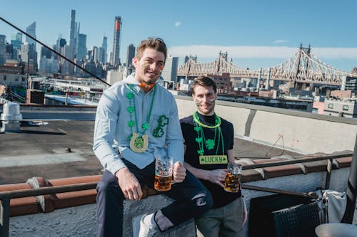 Smiling guys drinking beer while celebrating Feast of Saint Patrick on rooftop