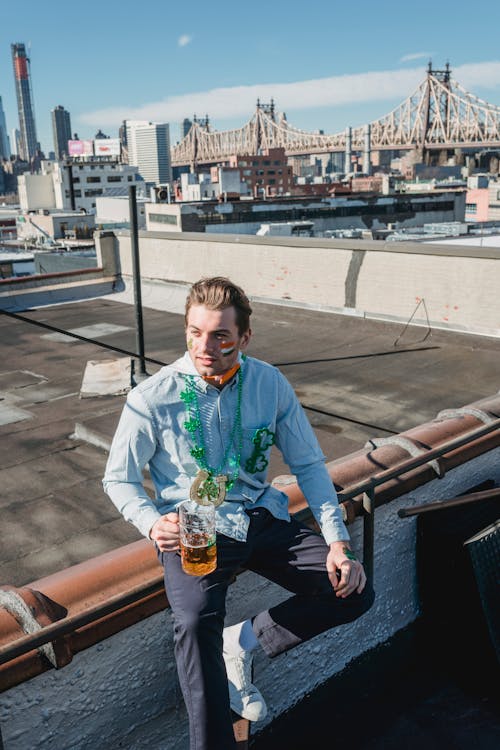 Trendy young man drinking beer while celebrating Feast of Saint Patrick on roof
