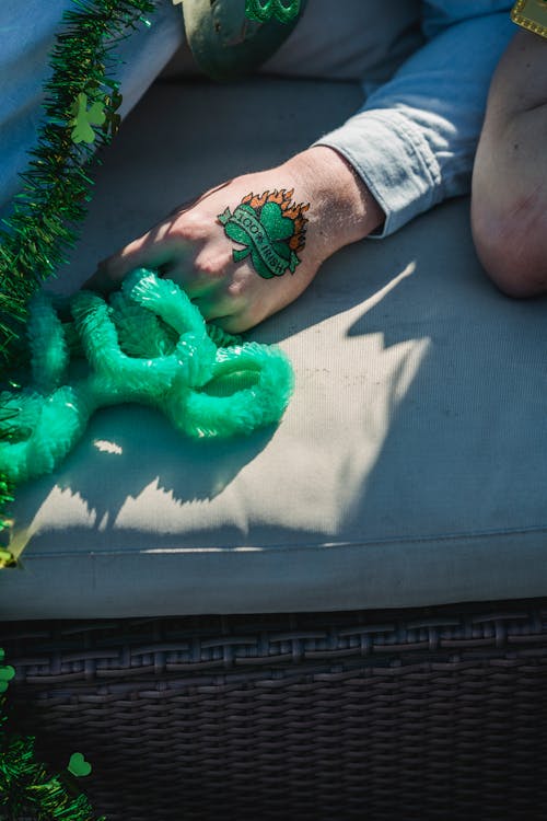 Crop anonymous man with clover tattoo on hand relaxing on sofa on terrace