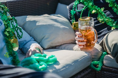 Crop anonymous men boozing beer on couch during outdoor party