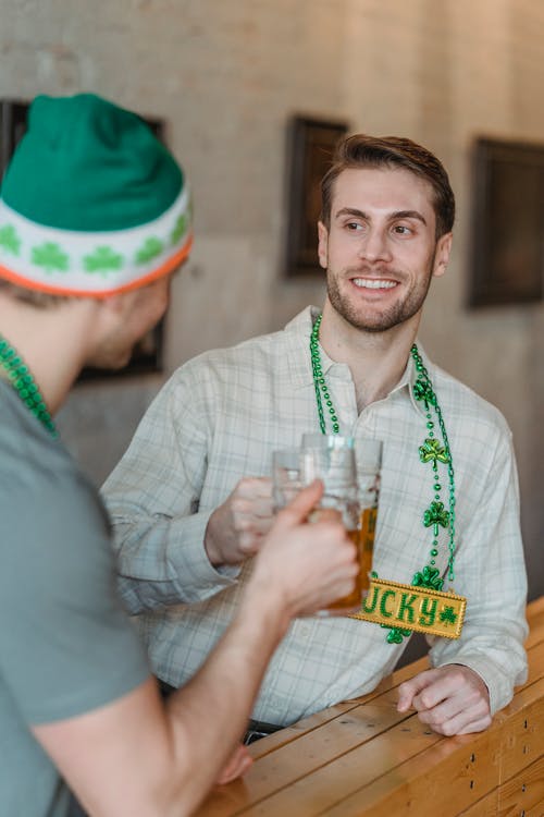 Happy young male raising mug of beer with friend sitting in pub and celebrating national holiday