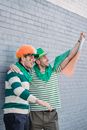 Side view of male friends wearing clown party wig and green stripe t shirt and green sparkle hat covered with irish flag greeting and celebrating Saint Patrick Day