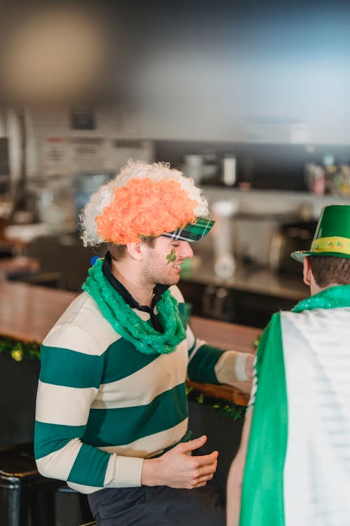 Side view of lively friends in national costumes and accessories devoted to Saint Patrick Day celebration having rest in bar