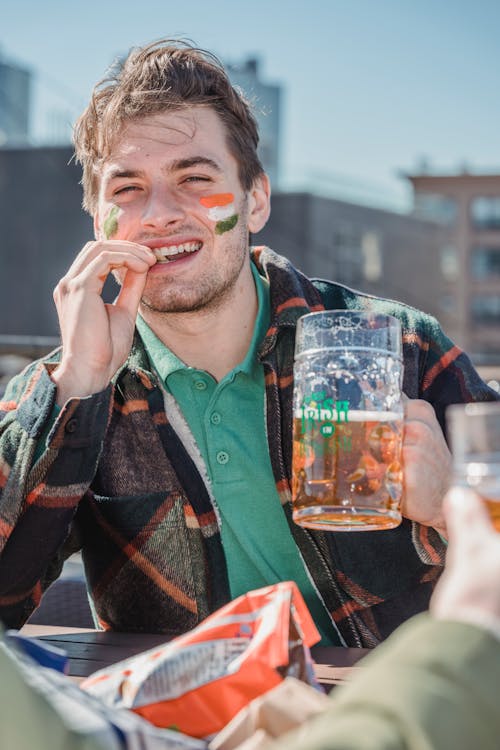 Young smiling man drinking beer and eating snacks on open air