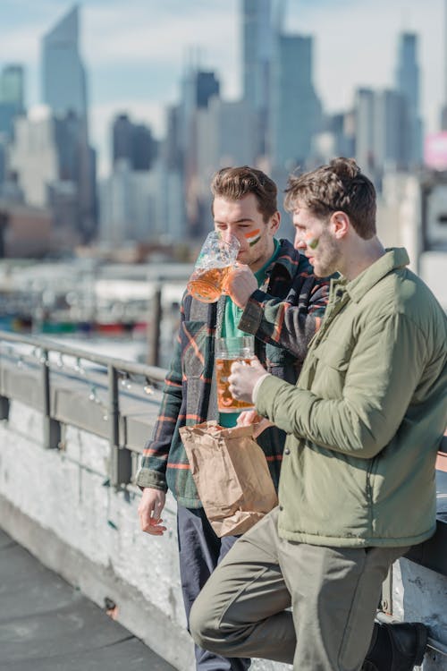 Fans of national team wearing warm clothes with national flag colors on cheeks drinking beer and eating fast food and staying in the street of modern city