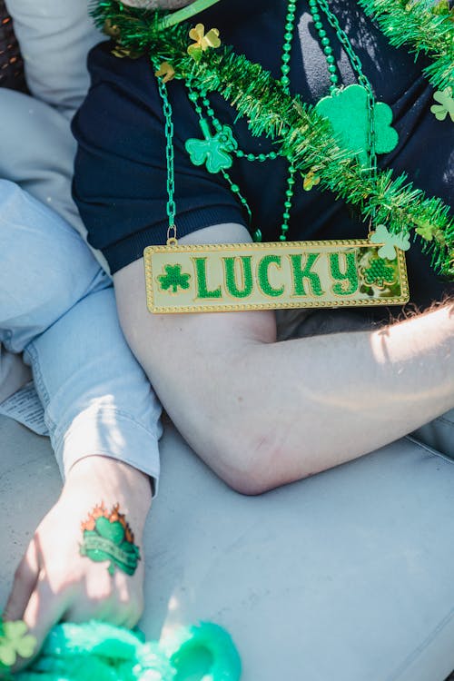 Free From above of crop anonymous male friends in casual clothes and festive shamrock accessories chilling on sofa during Feast of Saint Patrick Stock Photo