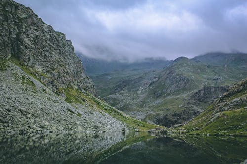 бесплатная Серые и зеленые горы с водоемом под пасмурным небом Стоковое фото