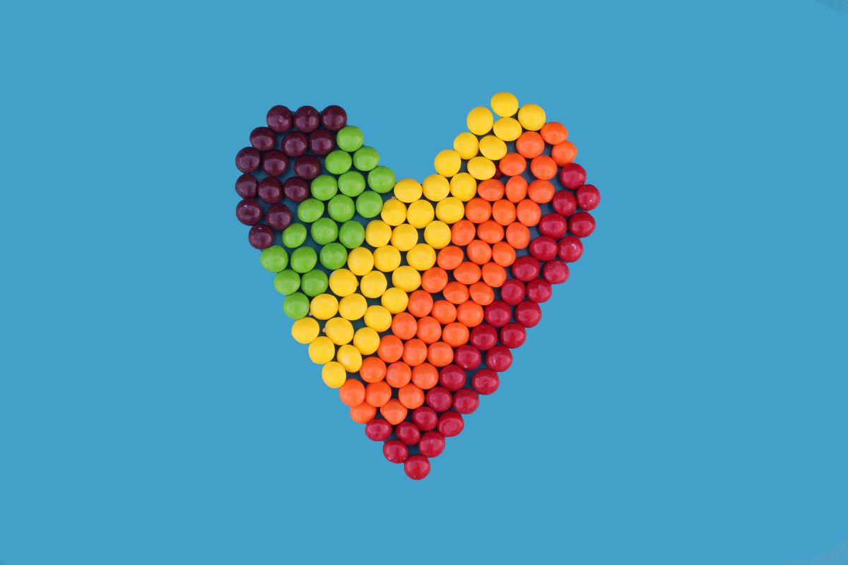 Rainbow-colored candies arranged in a heart shape on a blue backdrop, symbolizing love.