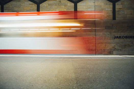 Long exposure shot capturing motion blur of a passing train in an underground station with Jakobi inscription.