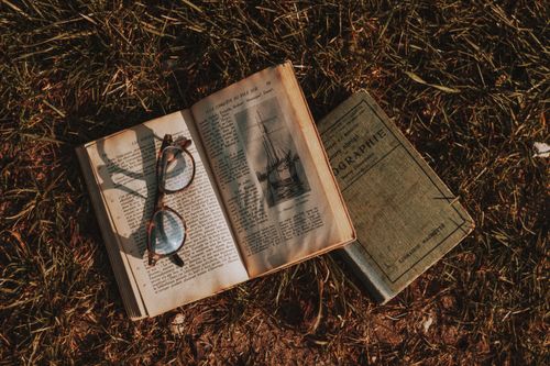 Free Top view of aged textbooks with illustration and eyewear on open page on meadow in sunlight Stock Photo