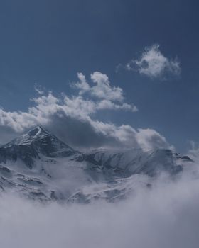 Dramatic aerial view of a serene, snow-capped mountain peak enveloped by clouds.