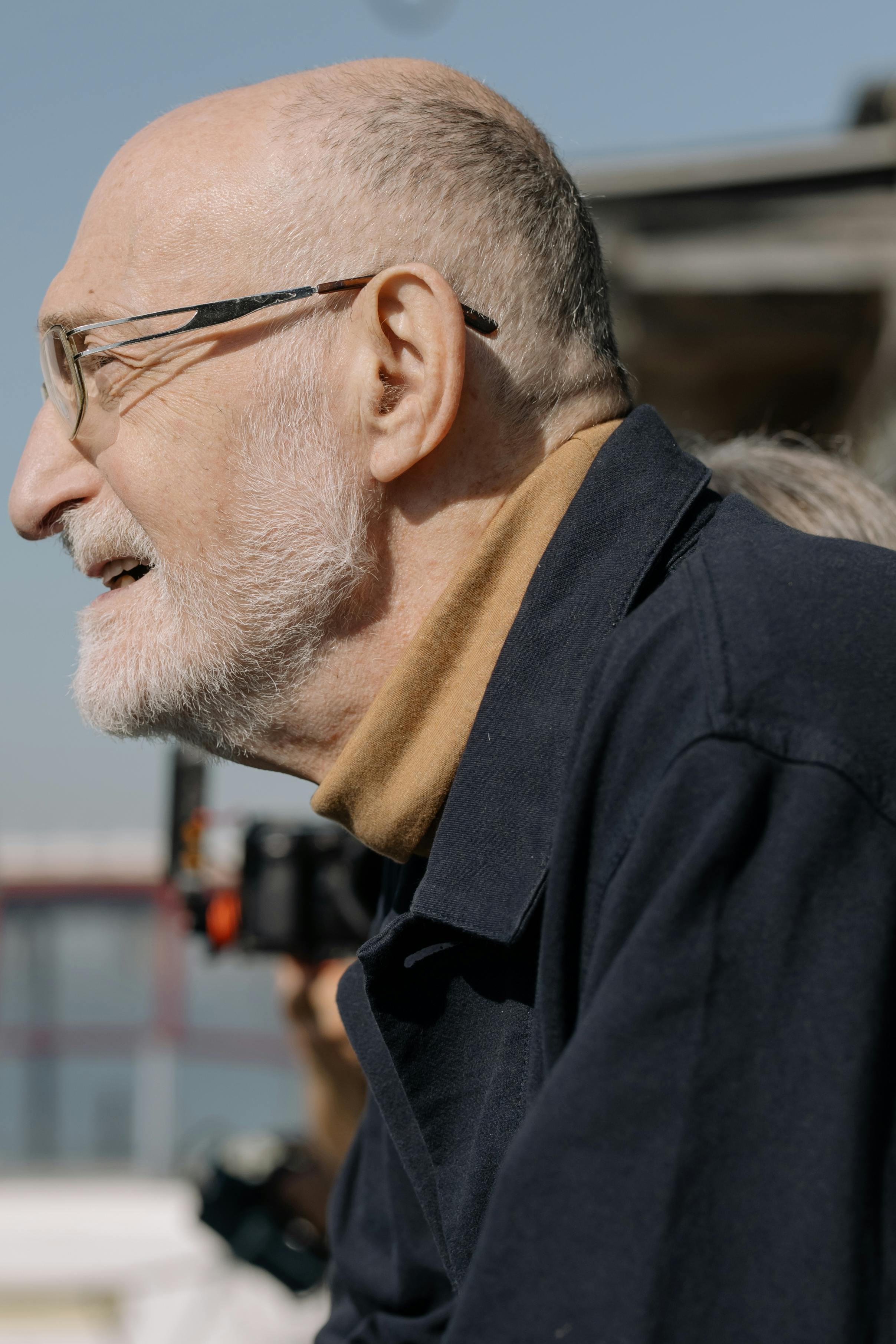 Elderly man in glasses and coat enjoying a sunny day outdoors.