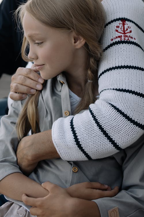 A Girl being Hugged by a Person Wearing a Knitted Sweater