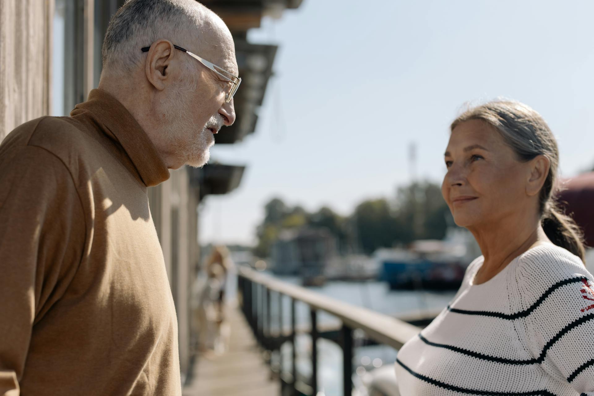 Senior couple smiling together by the water on a sunny day, enjoying leisure time.