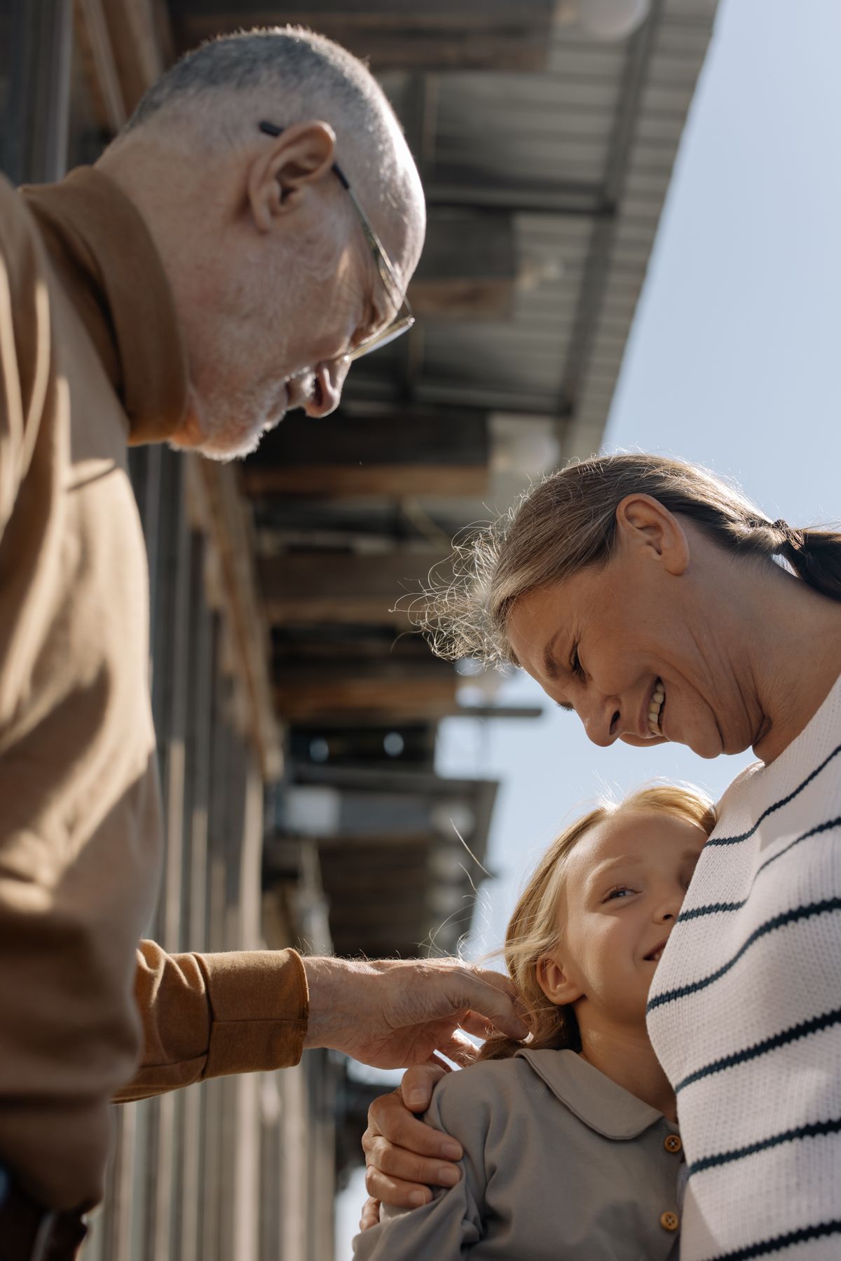 Grandparents hugging their granddaughter outdoors at golden hour.