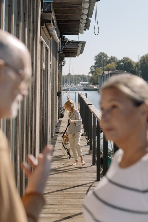 Free A child walks a dog on a dock while two adults share a conversation nearby. Stock Photo