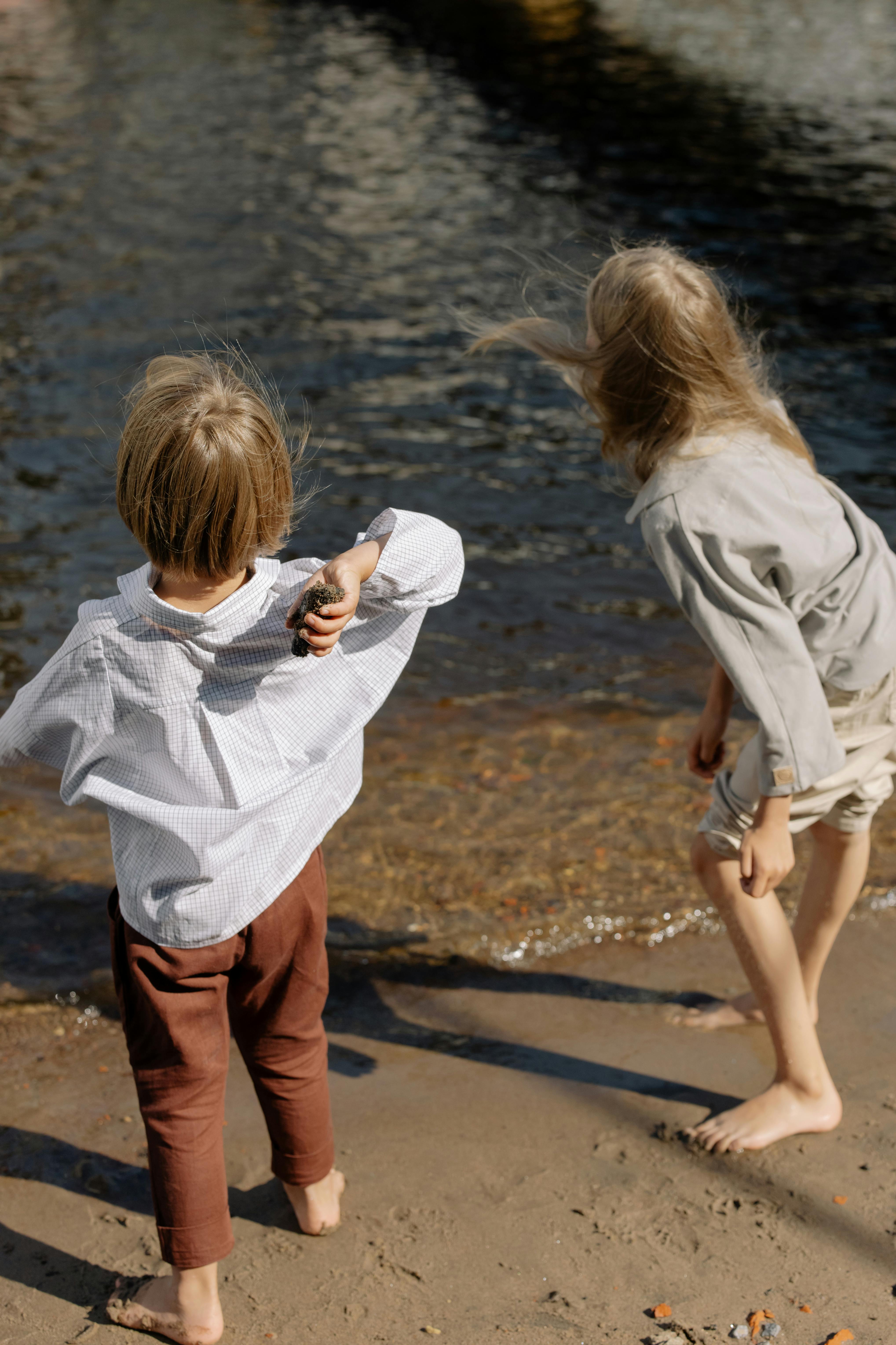 Two children enjoying a playful day at the beach, throwing stones by the water.
