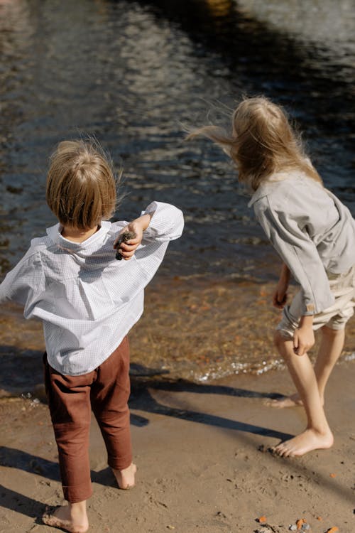 Free High-Angle Shot of Boy and Girl Throwing Rocks at the Beach Stock Photo