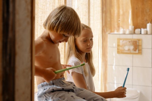 Free Brother and Sister Holding Their Toothbrushes Inside the Bathroom Stock Photo