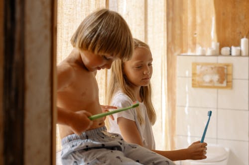 Brother and Sister Holding Their Toothbrushes Inside the Bathroom