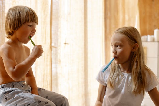 Two young children brushing teeth together in a sunlit bathroom, promoting good oral hygiene habits.