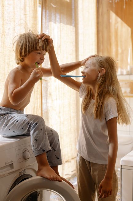 Deux enfants, un garçon et une fille, se brossant les dents ensemble devant un miroir, illustrant l'autonomie dans les routines quotidiennes grâce à la gestion du temps Montessori.