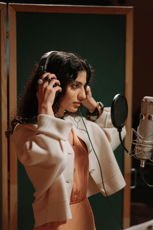 Free Female vocalist adjusting headphones while recording music in a studio. Stock Photo