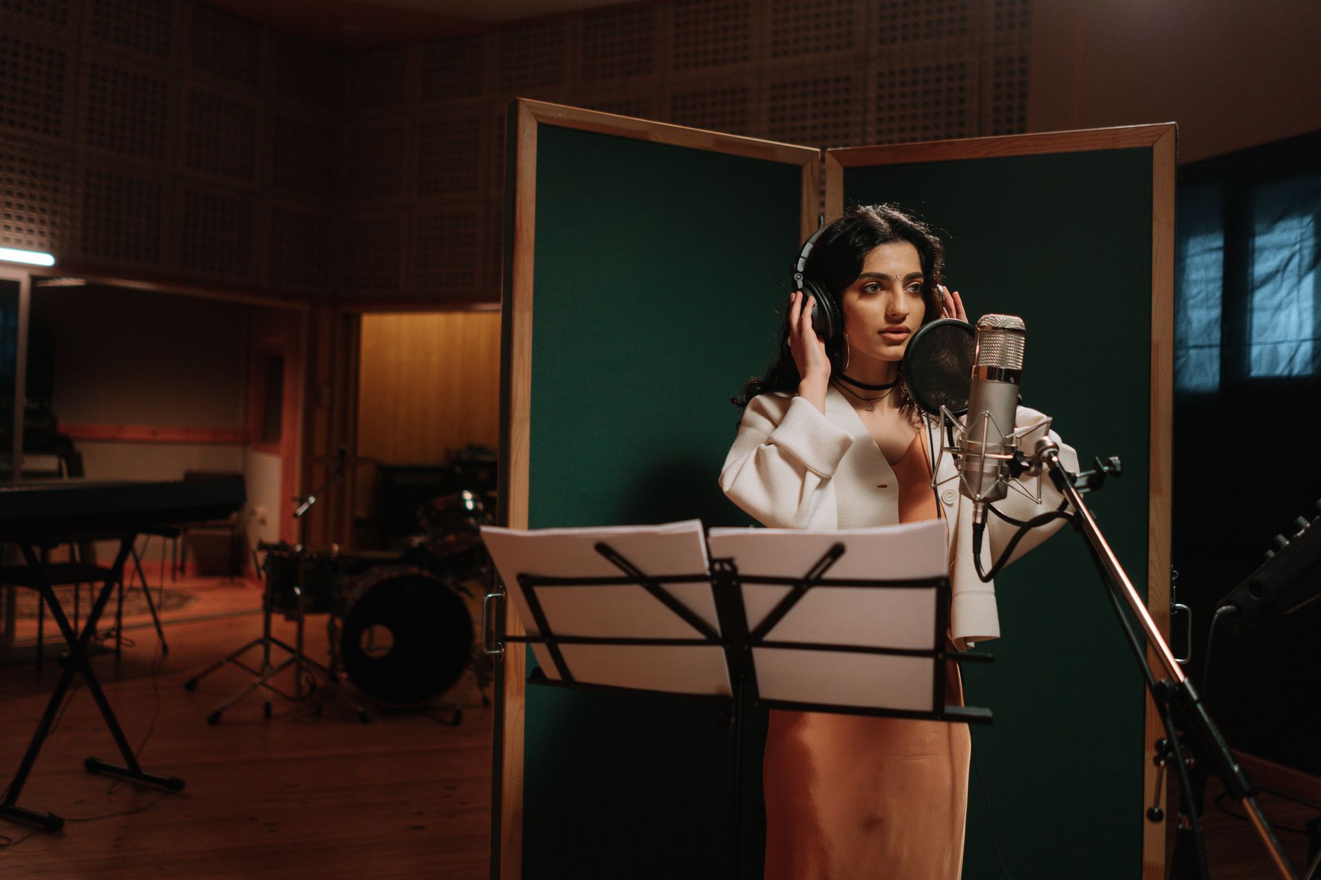 Woman singing into a microphone in a music studio with headphones.
