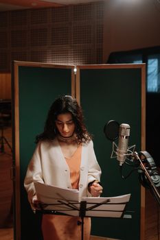 A female singer in a recording studio with microphone and music stand.